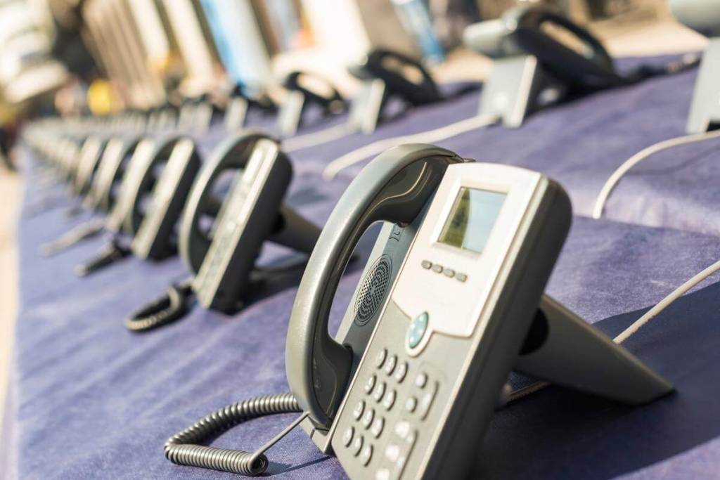 Why Consider a Multi-line Phone System_Many Phones in two straight rows. Large groips of telephones arranged in two lines on blue background indoors.